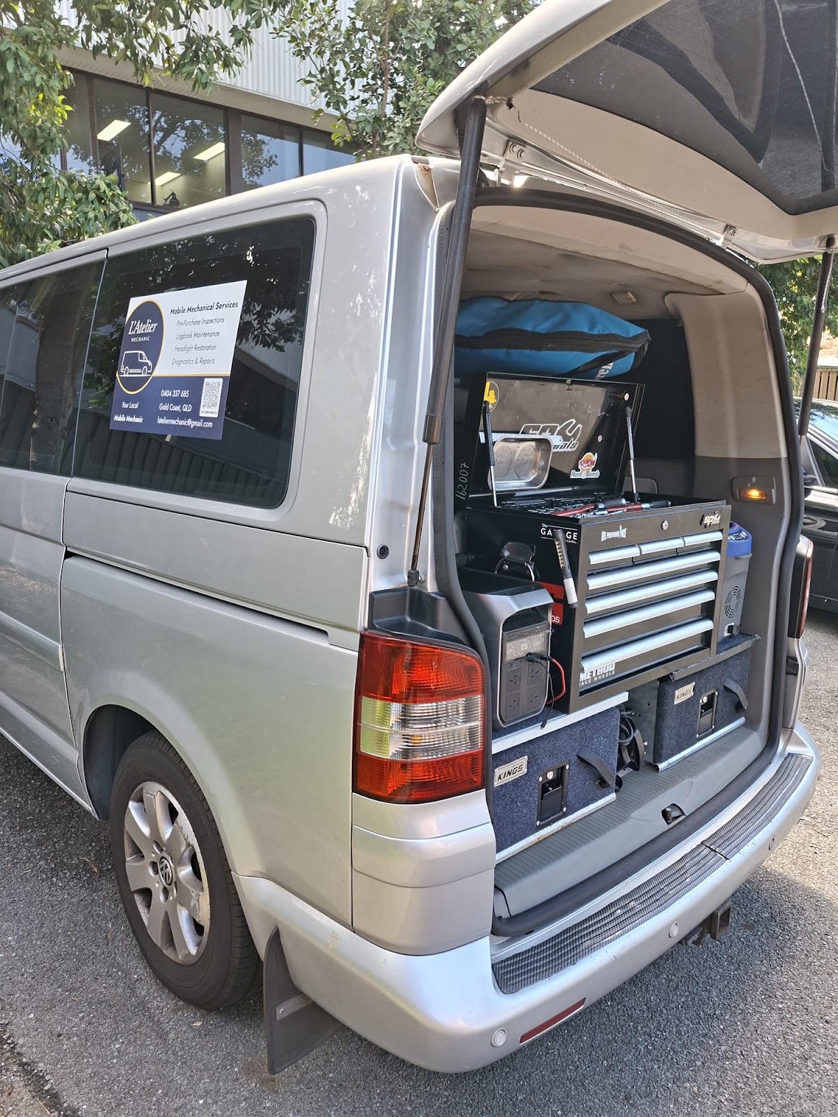 The silver van with the tailgate up, a tool chest and drawers fitted in the back and the L'Atelier sign in the window