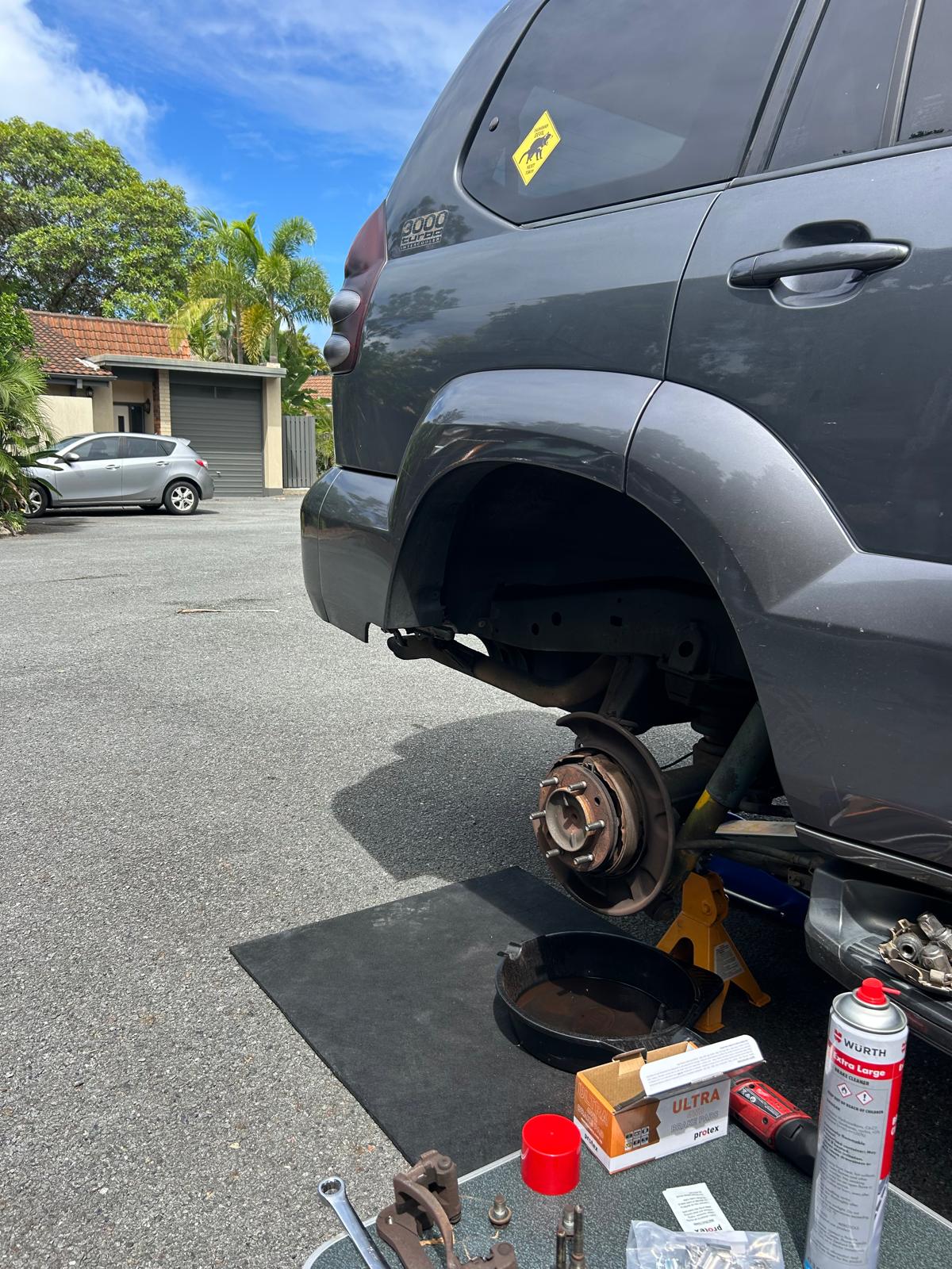 A 4WD up on stands in a driveway, the rear drum brake stripped and the parts laid out on a mat