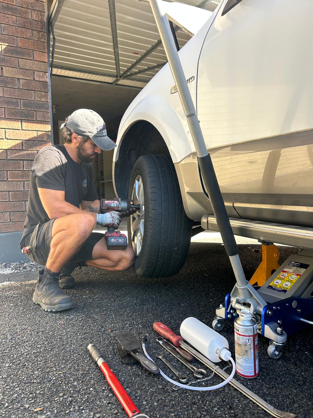 Nicolas in a cap and work shirt, fitting a wheel on a white 4WD with a trolley jack beside him