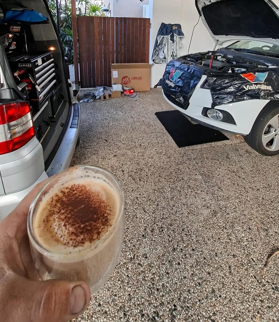A coffee in hand in a home garage, the van's drawers open on the left and a white hatch with the bonnet up on the right