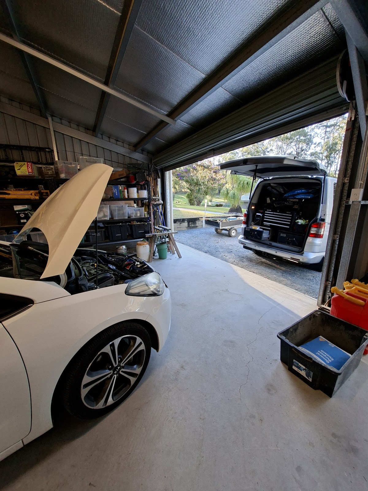 White car with the bonnet up in a home garage, the service van parked outside the roller door
